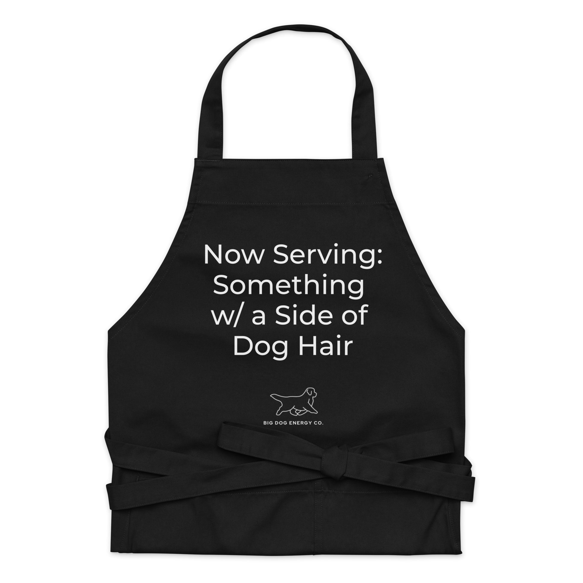 Black cooking apron with the saying "Now Serving: Something with a side of dog hair" in white text over a white Big Dog Energy Company logo