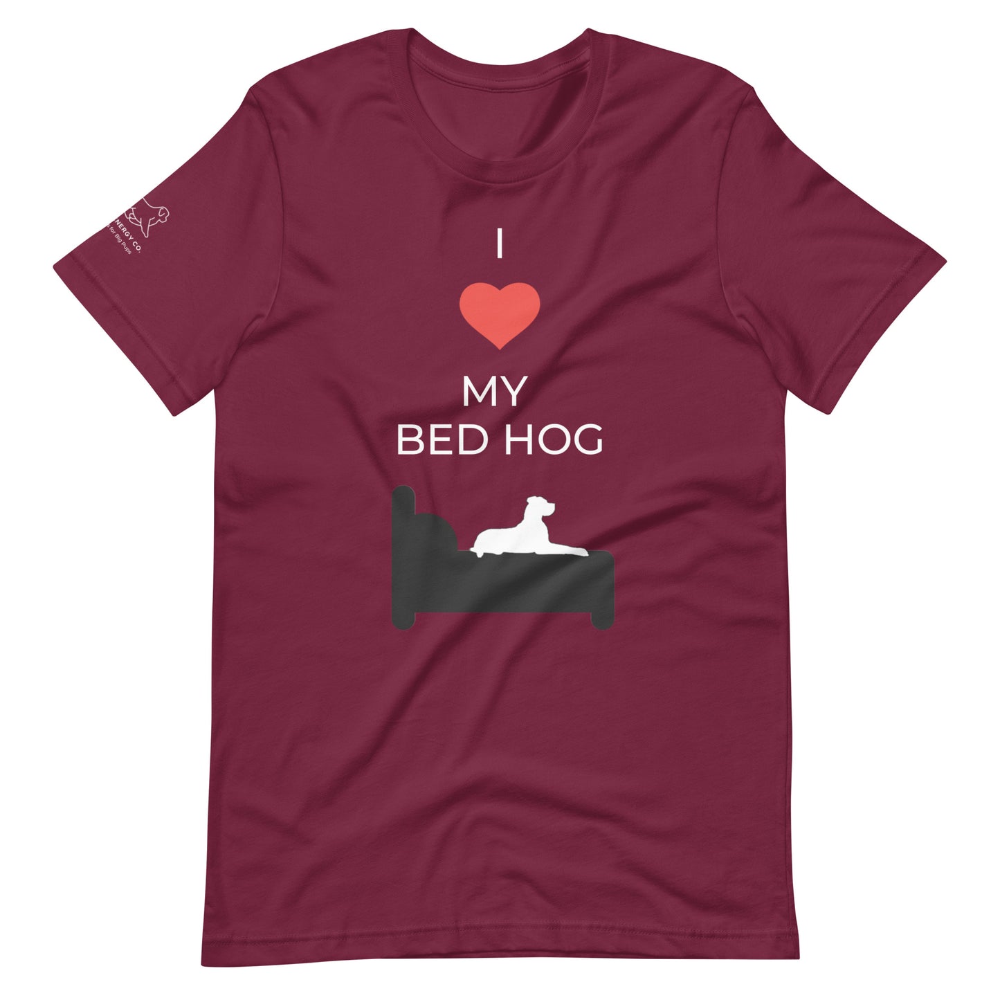 Front of a maroon t-shirt that reads "I love my bed hog" in white text over an illustration that is the white silhouette of a large dog laying on the dark silhouette of a bed. The word "love" is replaced by a red heart symbol.